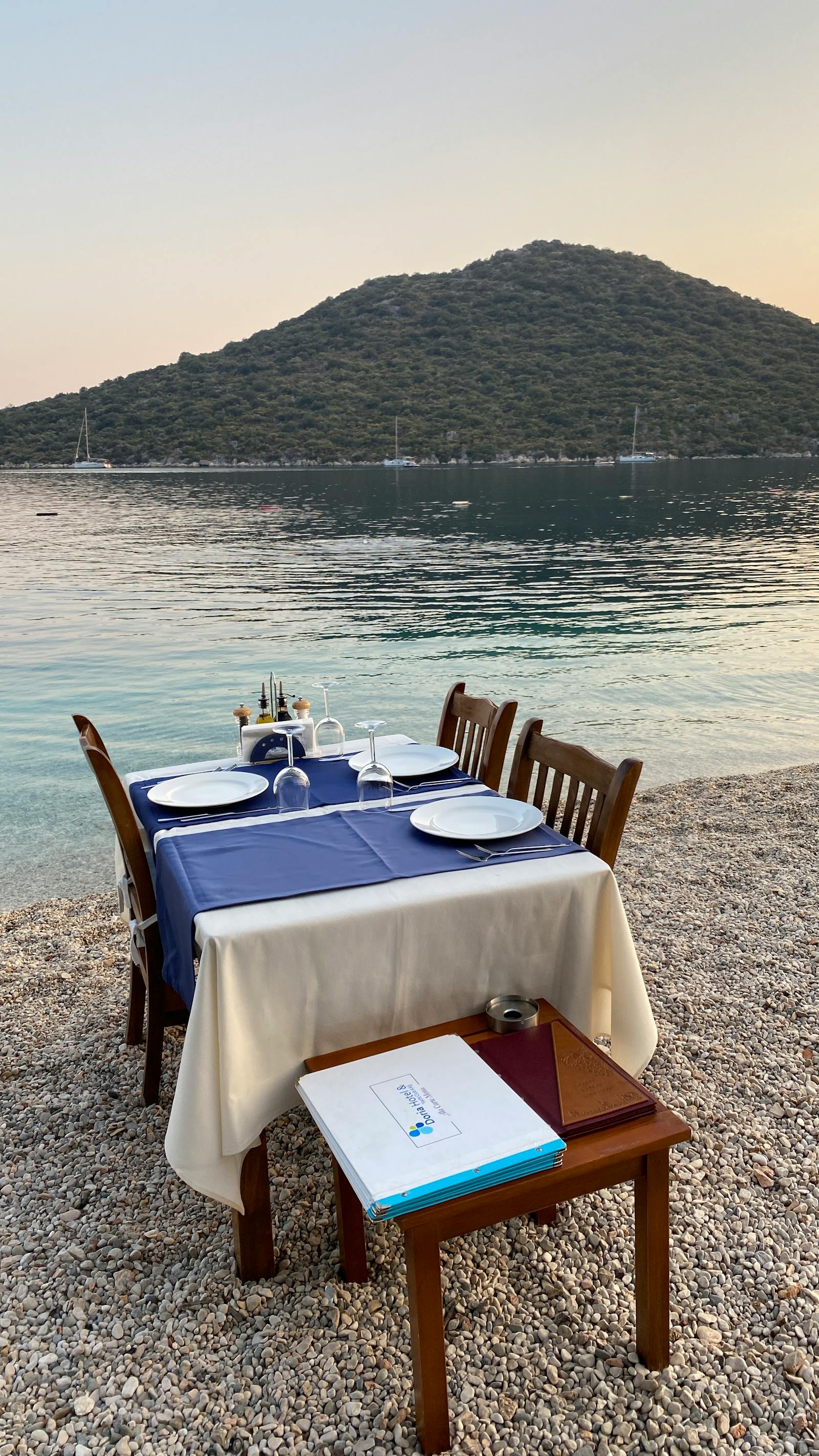 Seaside dining setup at La Petite, white linen tables on the Ionian pebbles
